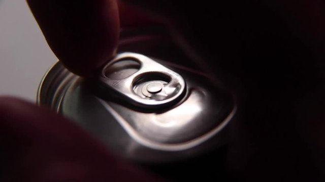 Macro footage of drink can being opened and picked up from table. Dark liquid visible in the can and around its edges.