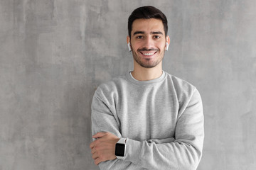 Portrait of smiling handsome man wearing smart watches, standing with crossed arms against gray textured wall