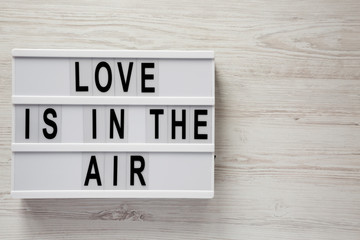 Lightbox with text 'Love is in the air' on a white wooden background. Valentine's Day 14 February. Copy space.