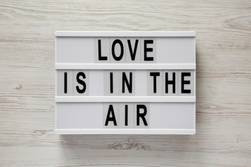 Modern board with text 'Love is in the air' on a white wooden background. Valentine's Day 14 February.