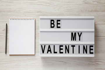 Obraz premium Lightbox with text 'Be my Valentine', blank notepad over white wooden surface. Valentine Day 14 February.