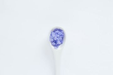 White decorative spoon with violet sea salts on the white background. Relaxing concept.