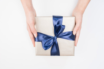 Woman's hands are holding present box with dark blue bow on a isolated background. Festive concept.