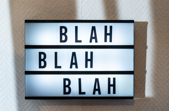 Message “blah blah blah” on illuminated board. Boring concept with text. Black letters blah-blah on white wallpaper wall.
