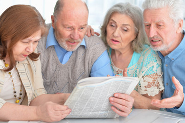 two senior couples sitting at table and reading newspaper