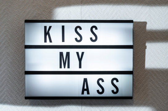 Message kiss my ass on illuminated board. Welcoming concept with text. Daylight from window.