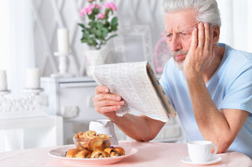 Emotional senior man  reading newspaper at home 