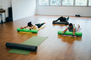 Naklejka premium People doing exercises with foam rollers in the gym