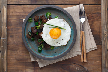 Sunny side fried egg with croutons and herbs, close view