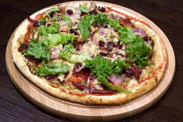  meat pizza with greens on a table in a wooden plate
