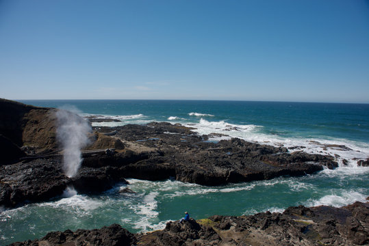 The Spouting Horn at Cape Perpetua on the Oregon Coast. A man watching the feature across a inlet of water.