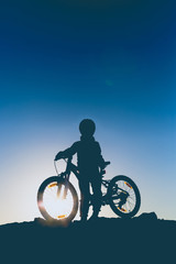 Naklejka premium Silhouette of a little girl with a bicycle at sunset