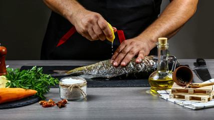 Add lemon juice to fish carp in chef hands, black background. Food recipe photo, copy text