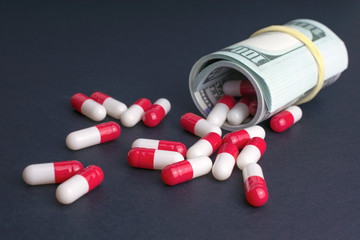 biotech and pharmaceutical companies. red white capsules spill out of folded dollars, dark background