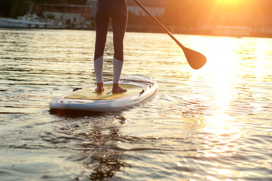 SUP silhouette of young girl paddle boarding at sunset