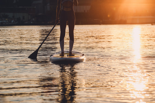 SUP silhouette of young girl paddle boarding at sunset