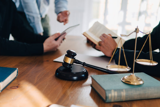 Business Man And Lawyers Discussing Contract Papers With Brass Scale On Wooden Desk In Lawyer Office.