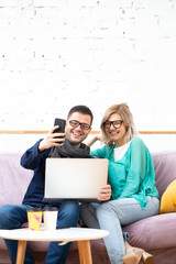 Friends sit on the couch, chatting and using a smartphone, desktop computer.