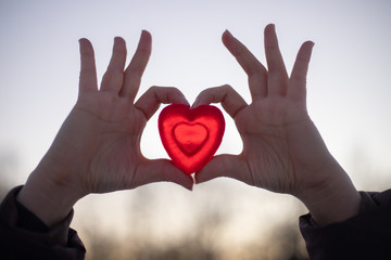 A girl holds with two hands a heart symbol from glycerin of a red heart in the street in clear frosty weather.