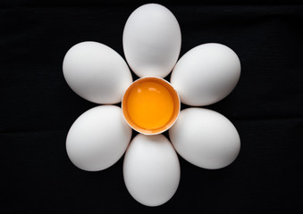 Chicken white eggs laid out around a broken egg in the form of a chamomile on a black background. Easter