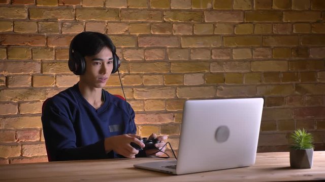 Closeup portrait of young attractive korean man in headphones playing video games indoors