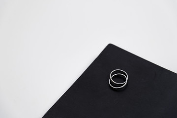 White gold or silver crossing ring on black cover of notebook lie on white table background.