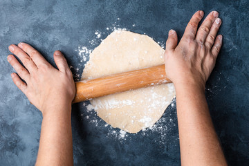 Female hands rolling dough on a table with a wooden rolling pin. Top view. Flat lay.