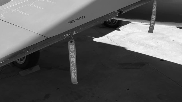 REMOVE BEFORE FLIGHT red ribbon tags on wing of military fighter jet. F-104 Starfighter. Black and white. Handheld shot with stabilized camera.