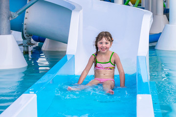 A little girl is riding down the slides in the water park. Funny children's attraction in the pool....