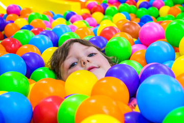 Fototapeta na wymiar A little girl bathes in colorful plastic balls. Children's attraction. Fun for kids.
