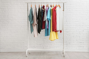 Wardrobe rack with stylish clothes near brick wall indoors