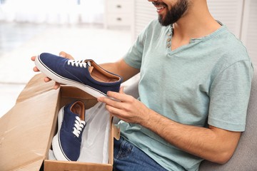 Young man opening parcel with shoes at home, closeup