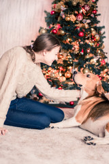 girl smiling and petting her dog in front of a christmas tree