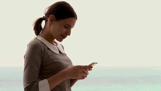 Young businesswoman standing with smartphone on terrace, with sea view
