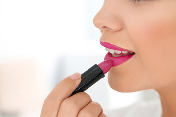 Obraz premium Beautiful woman applying lipstick on light background, closeup