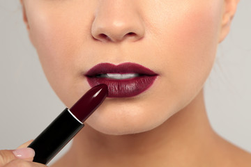 Beautiful woman applying dark lipstick on gray background, closeup