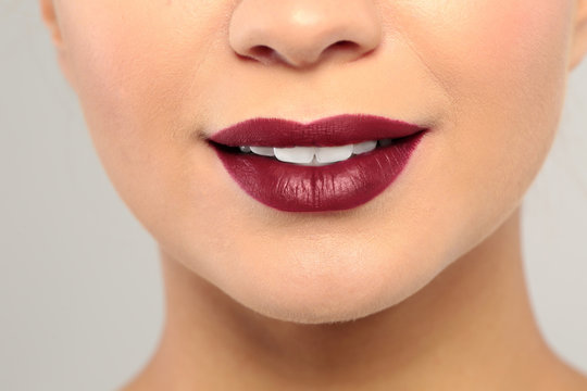Young woman wearing dark lipstick on gray background, closeup