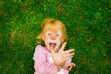 beautiful little girl at the children's party with a butterfly pattern on her face, posing emotionally while lying on the bright green grass