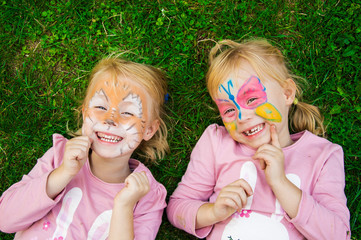 two little girls with colorful painted faces having fun on the grass