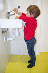 3 years child boy washing hands at adapted school sink but he reaches hardly to the faucet