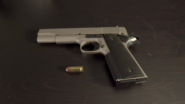 Cocked pistol with .45 ACP cartridge laying on table, wide center shot