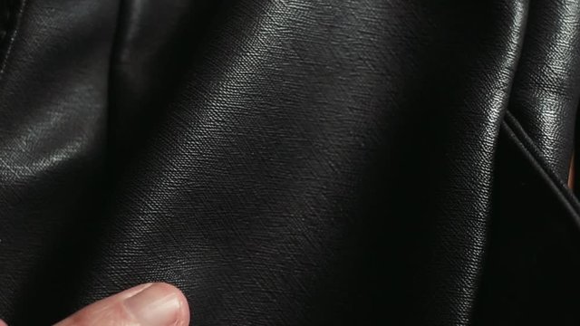 The hand of a man checks to touch the quality of a black natural or artifical leather bag.