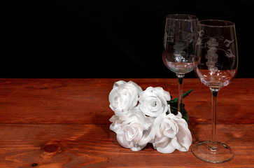 Beautiful etched wine glasses with awhite roses on wooden table and dark background.
