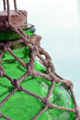 Close up of the top of a bright green hand-blown rippled antique glass net float or jar with cork stopper hung in a knotted jute or hemp rope macrame knotted hanger against white background.