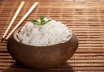 Cooked white rice in wooden bowl with chopsticks on the wood brown bamboo background.