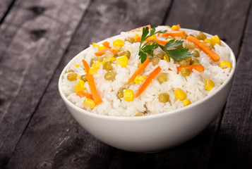 Cooked white rice with vegetables in a bowl on the wood black background.