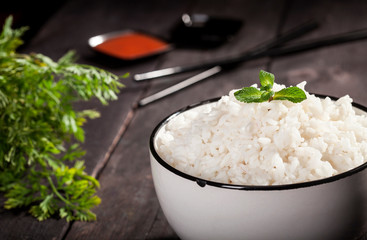 Cooked white rice in a bowl with sauces and chopsticks on the wood black bamboo background.