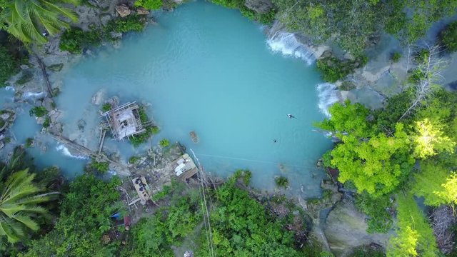Vertical aerial shot of a turquoise pond surrounded by jungle and palm trees - Cambugahay Falls, Siquijor, Philippines.