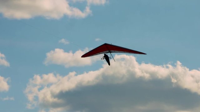Hang glider being towed past puffy white clouds