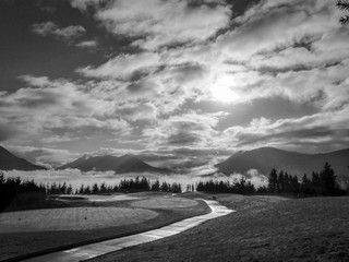Black & White Photo of a Golf Course on a Cloudy Day - with a Cart Path and Driving Tees and a Foggy Mountain Range in the Background